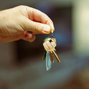 A close-up image of a hand holding a keyring with several house keys, symbolizing real estate and home ownership.