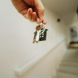 Close-up of a hand holding a keychain in the shape of a house, symbolizing real estate and property ownership.