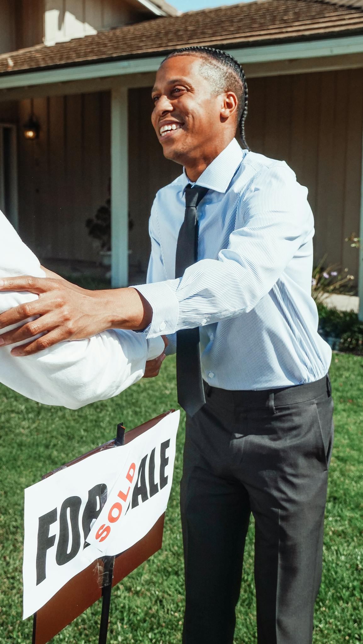 Man shaking hands outside a house with a 'Sold' sign, marking a successful real estate transaction.