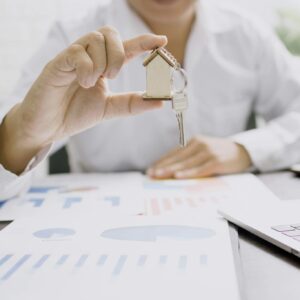 Real estate professional presenting a house model with keys, symbolizing property investment and ownership.